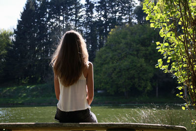 Rear view of woman sitting on bench by lake