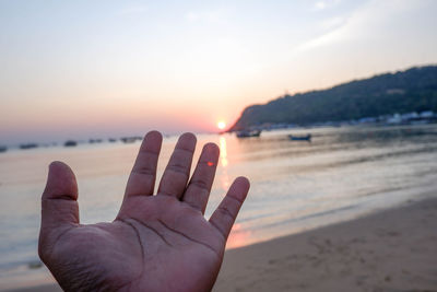 Close-up of hand against sea during sunset