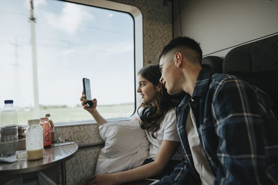 Sister sharing smart phone with brother while doing photography in train