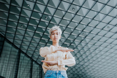 Portrait of young woman gesturing equal sign while standing against ceiling