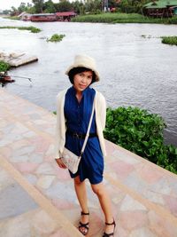 Portrait of young woman standing on steps by river at park