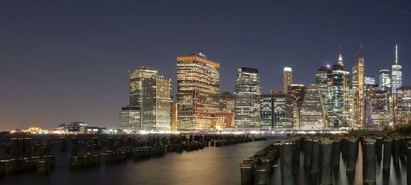 Illuminated buildings by river against clear sky at night