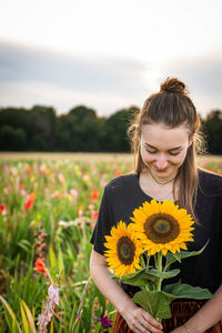 Portrait of young woman with yellow flowers on field