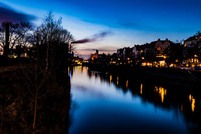 River by illuminated city against blue sky at dusk
