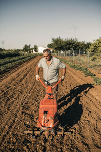 Male farm worker plowing land through harrow during sunny day