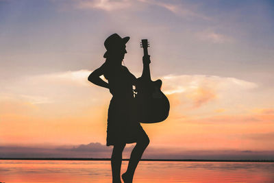 Side view of woman standing on beach against sky during sunset