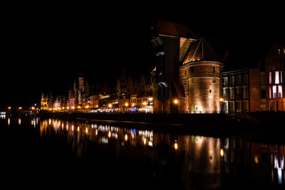 Illuminated buildings by lake against sky at night