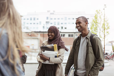 Smiling male and female students standing with friends at university campus