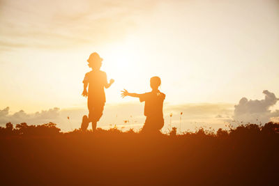 Silhouette people standing on field against sky during sunset