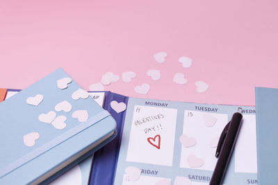 Heart-shaped confetti and calendar on pink background