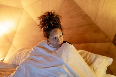 Woman sitting in bed wrapped in sheets.