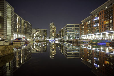 Illuminated buildings by river against sky at night