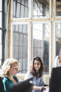 Smiling female computer programmer looking at coworker while working in creative office