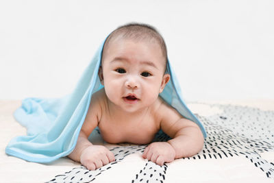 Asian baby under the towel after bathing lying on bed under blue towel,portrait of a crawling baby.