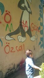 Rear view of boy standing against graffiti wall