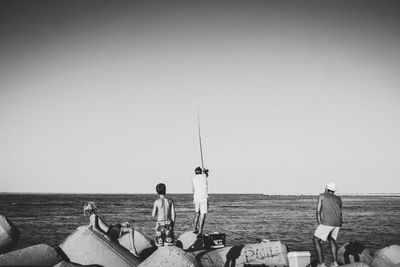 People fishing in sea against clear sky