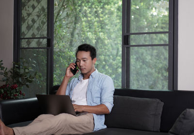 Young man using mobile phone while sitting on window