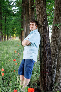 Portrait of man standing by tree trunk in forest