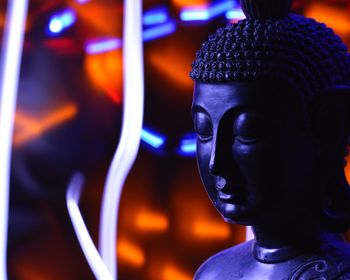 Close-up of buddha statue against illuminated abstract backgrounds