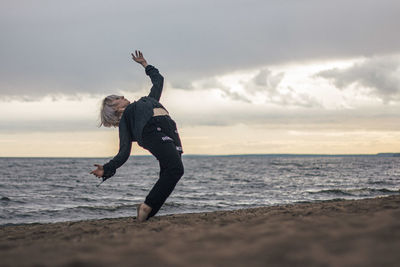 Full length of woman dancing on beach against sky