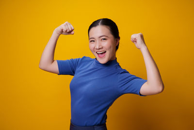 Portrait of smiling young woman against yellow background