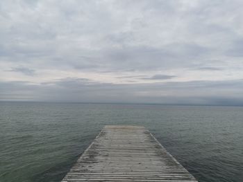 Pier on sea against cloudy sky