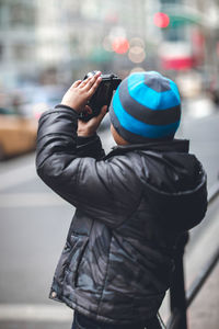 Side view of boy photographing on street using camera