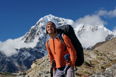 Smiling tourist with a backpack stands in front of a white mountain.