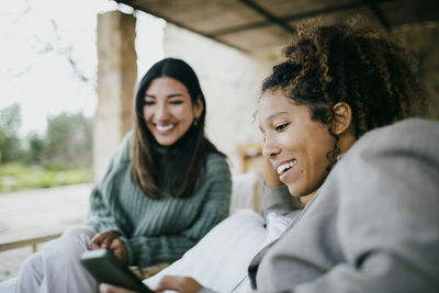 Happy woman sharing smart phone with friend at backyard