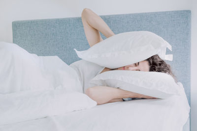 Woman covering ears with pillows while sleeping on bed