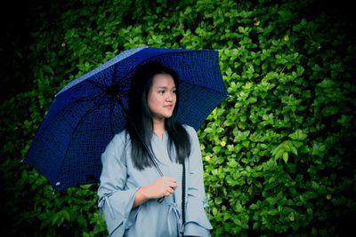 Young woman holding umbrella while looking away against plants in park