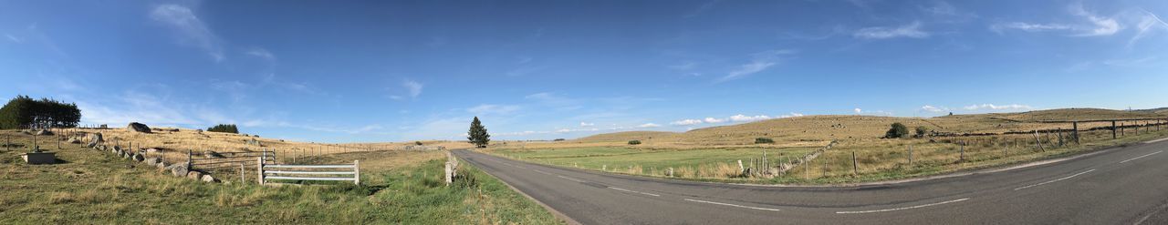 Panoramic view of road amidst field against sky