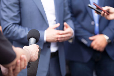 Midsection of people holding mobile phones and microphone