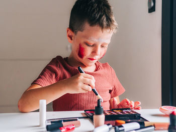 Charming child with makeup applicator looking away at table with eyeshadow palette