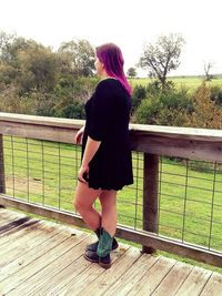 Rear view of woman standing by railing against trees