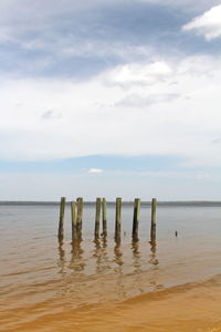 Wooden posts in sea against sky