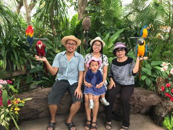 Full length portrait of smiling family with birds sitting at park