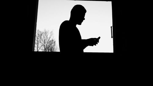 Silhouette of man using smart phone against sky