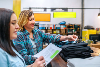 Happy woman checking price label of black pants next to her colleague on second hand clothing store