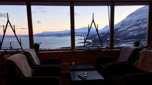 Chairs and table by sea against sky seen through window