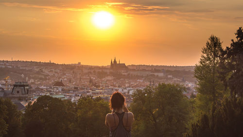 Rear view of man looking at cityscape during sunset