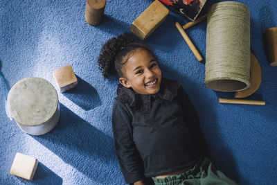 Portrait of smiling girl with toys lying on carpet at child care center