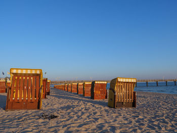 Wooden chairs on beach against clear blue sky