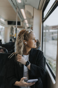 Businesswoman listening to music while sitting with smart phone in train