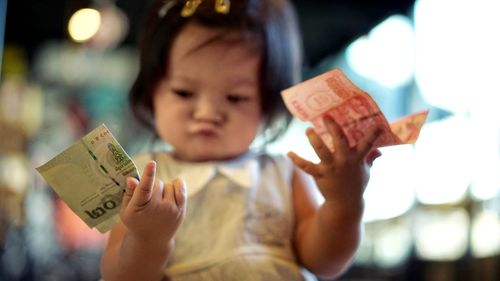 Close-up of girl holding money while sitting indoors