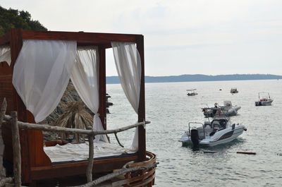Cabana bed with canopy and white curtains with a view on a sea with a speed boat in summer