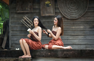 Smiling woman holding friends hair while sitting outside house