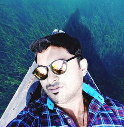 High angle portrait of man wearing sunglasses lying in boat on sea