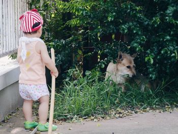 Boy with stick looking at dog against plants