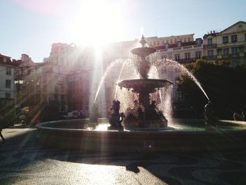 Fountain in city against sky on sunny day